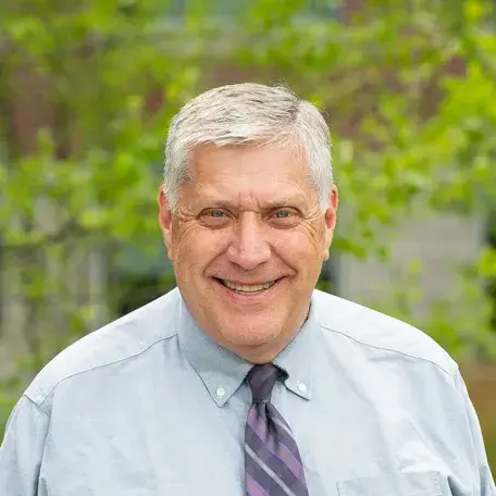 A person wearing a shirt and tie standing in front of a tree