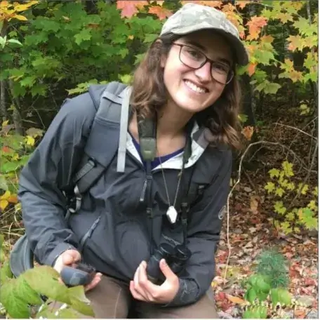 Morgan kneeling on the forest floor holding a GPS