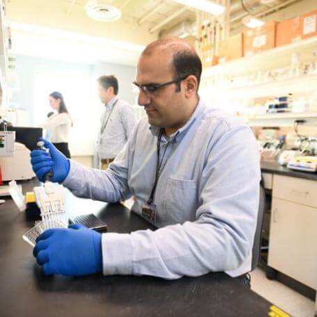 Person pipetting at a bench in a lab with two other researcher in the background