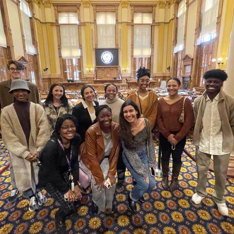 A big group of students from Kennesaw State University poses smiling for a photo at the Georgia statehouse.