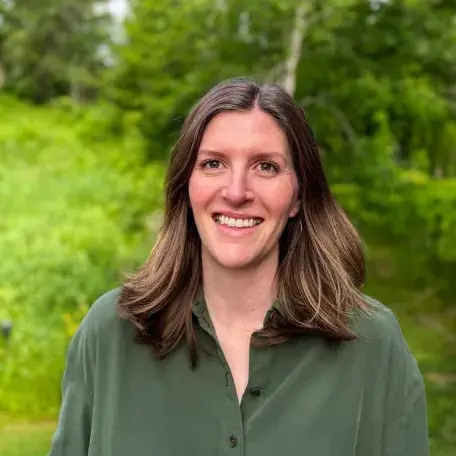 Headshot of Alayna Howard, wearing a green shirt, standing outside, smiling