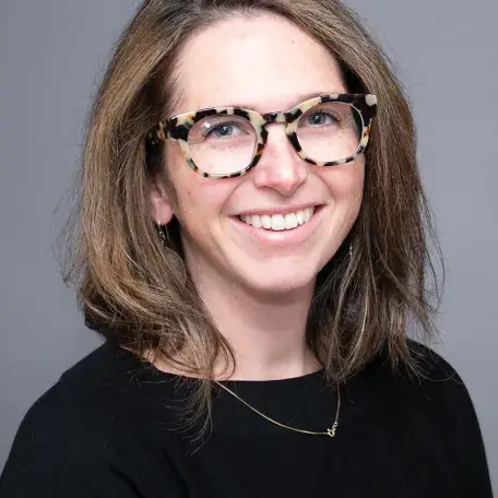 A person with brown hair and glasses wearing a black shirt