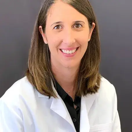 A person with brown hair wearing a white coat