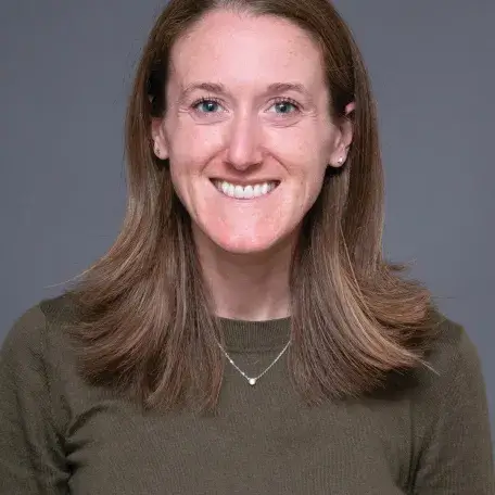 A person with long hair wearing a necklace and a brown shirt