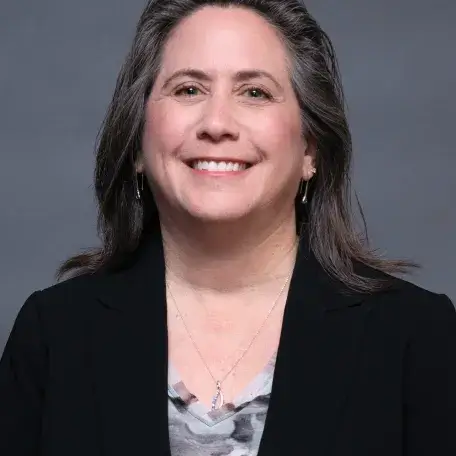 A person with brown hair wearing a black blazer and a gray shirt