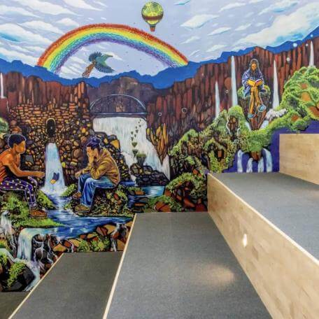 A beautiful, colorful mural painted along a set of stairs. The image shows people reading and engaged in a game together against a brackdrop of a forested waterfall and rainbow.