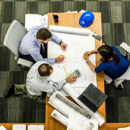Three people sit around a table in an office, looking at a blueprint.