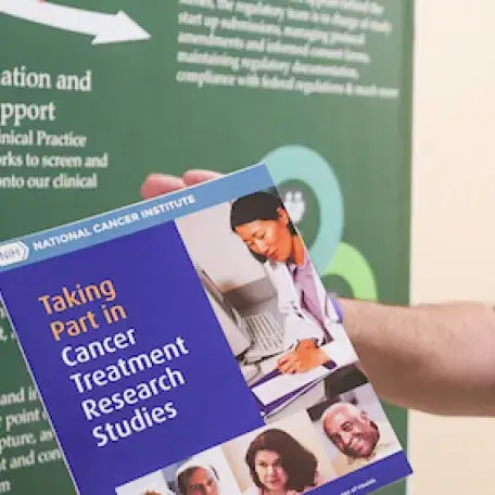 Person holding a pamphlet in front of a green poster board