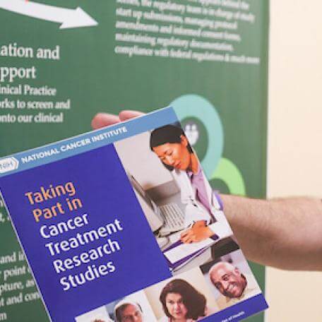 Person holding a pamphlet in front of a green poster board