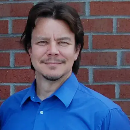 A person wearing a blue shirt standing in front of a brick wall 
