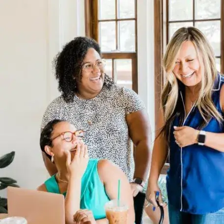 three people laughing while looking at a laptop
