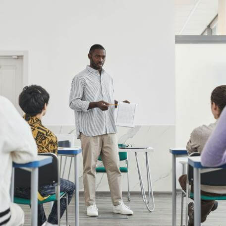 A Black professor lectures to adult students seated in desks