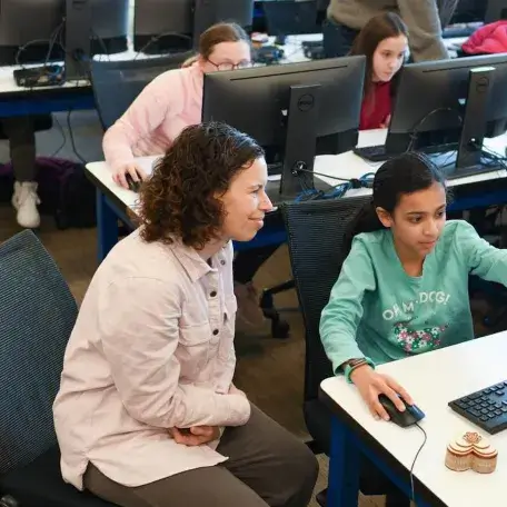 student pointing to a screen in front of a teacher
