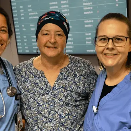 Three people, two wearing scrubs, smile at the viewer