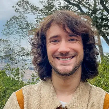 Person smiling outdoors with city in background.