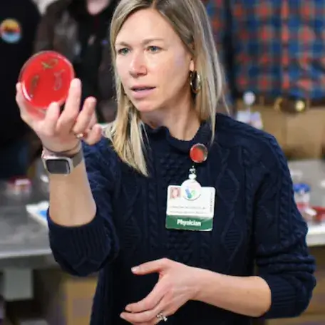 Individual with long blond hair holding a red agar plate to view the sample growth on the plate