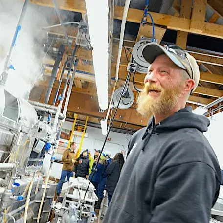 bearded, laughing Wade in ballcap in front of steaming evaporator