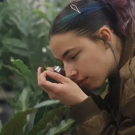 a young woman peers through a hand lens at a leaf
