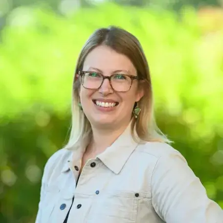A smiling woman in front of greenery.
