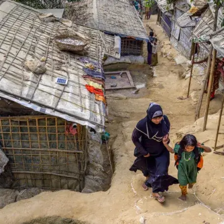 Ramshackle tents and buildings. A woman and child walk through. 