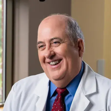 light skinned man with short gray hair wearing a white doctors coat