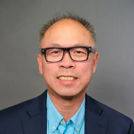light skinned man with glasses, short gray hair wearing a blue shirt and black blazer