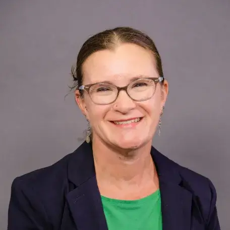 light skinned woman with glasses, brown hair pulled back, a green shirt and black blazer