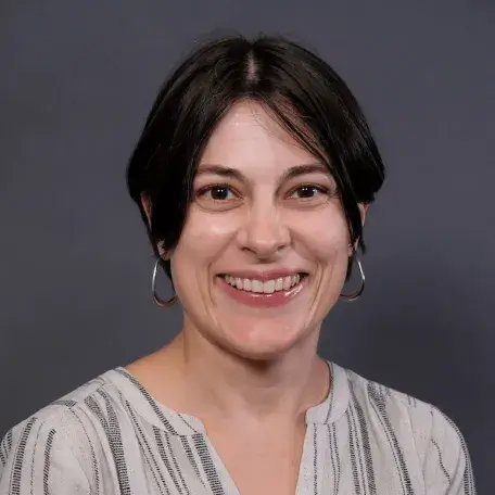 Black haired woman smiling, wearing large silver hoop earrings and an off-white and black striped linen blouse.  