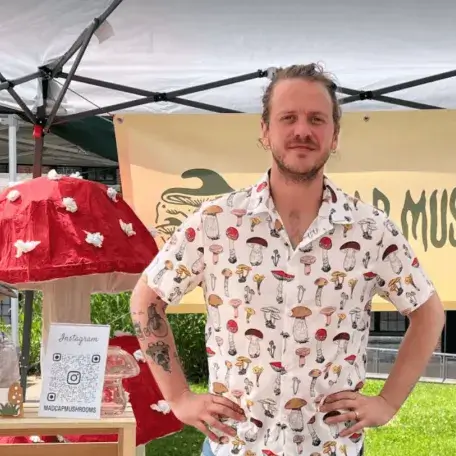 A young man standing at a mushroom stand at a farmer's market