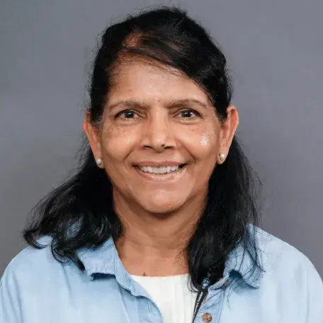 Woman with long black hair wearing a white knit blouse under a light blue button down shirt.