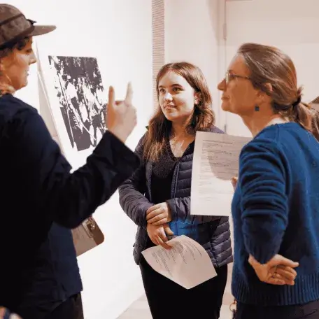 Two students discuss an artwork with a faculty member in the Fleming's Learning Studio.