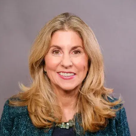 light skinned woman with long blonde hair and a emerald green jacket