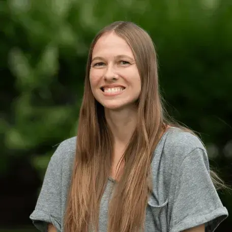 A photo of Colleen McGilpin, smiling and standing outside with a lush background.