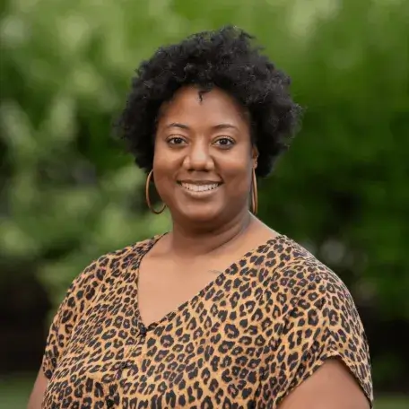 A photo of ShaRhonda Stevenson, smiling and standing outside with a lush background.