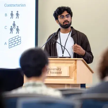 A graduate student addresses an audience with a presentation projected in the background
