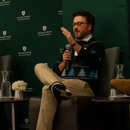 Evan DesLauriers speaks into a mic while sitting on stage