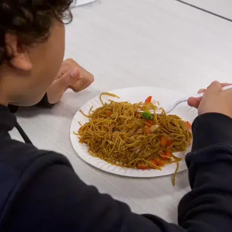 young child eating from a plate of noodles with vegetables