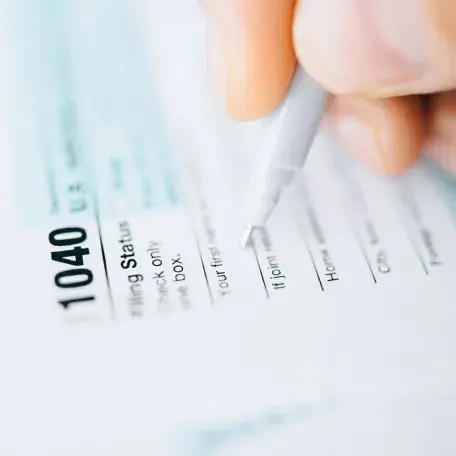 closeup of a hand filling out a 1040 form with a pen