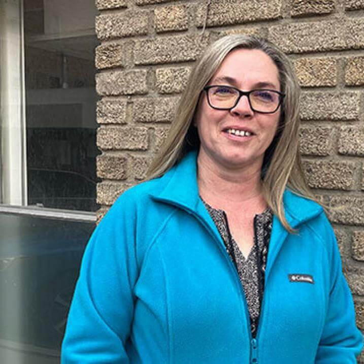 woman wearing glasses and blue jacket in front of brick wall