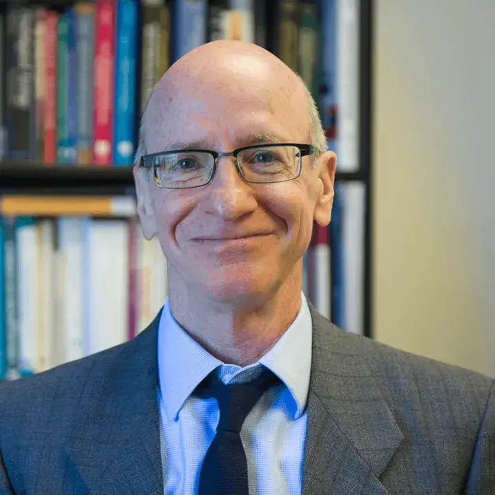 Tim, smiling, in an office type setting, with a book lined shelf behind him