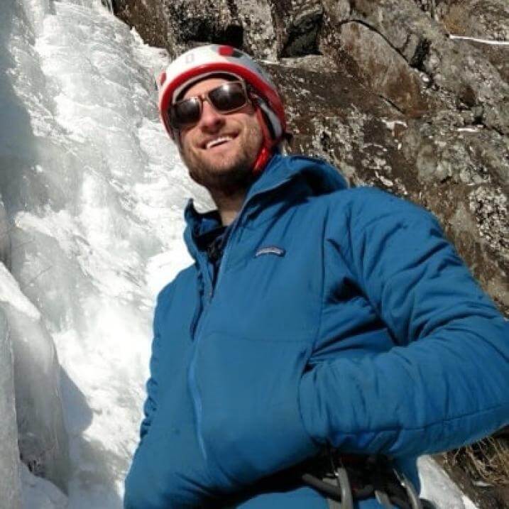 Photo of Devin in his climbing gear, smiling on the side of a rock face