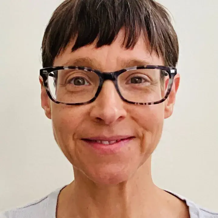 Freda standing in front of a white backdrop, smiling and wearing glasses.