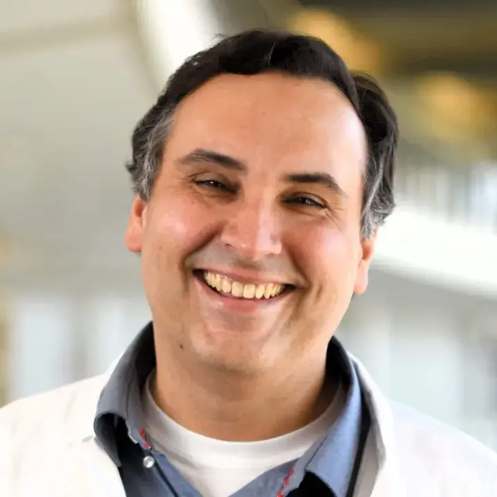 Headshot of a researcher and doctor in a white coat against a blurred indoor background.