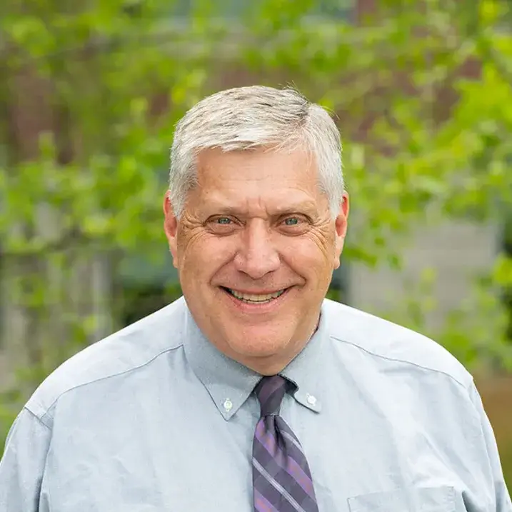 A person wearing a shirt and tie standing in front of a tree