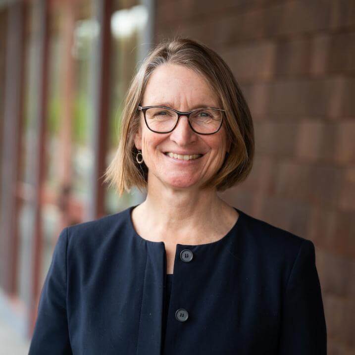 Susan, a woman with short light brown hair and glasses, smiling in an outdoor headshot.