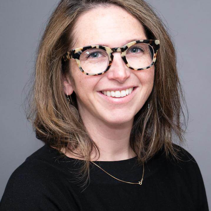 A person with brown hair and glasses wearing a black shirt