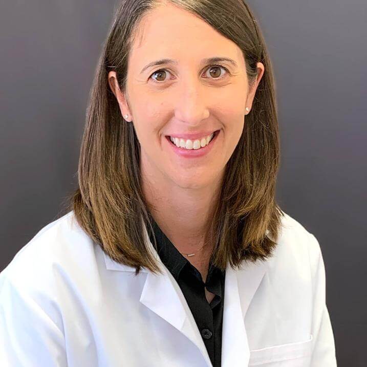 A person with brown hair wearing a white coat