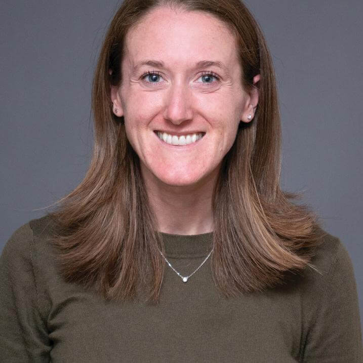 A person with long hair wearing a necklace and a brown shirt