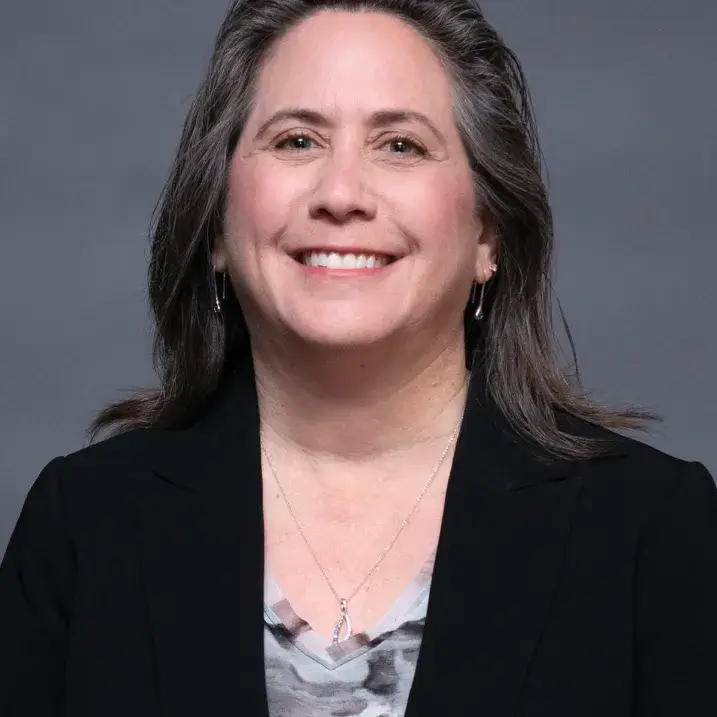 A person with brown hair wearing a black blazer and a gray shirt