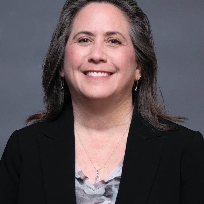 A person with brown hair wearing a black blazer and a gray shirt